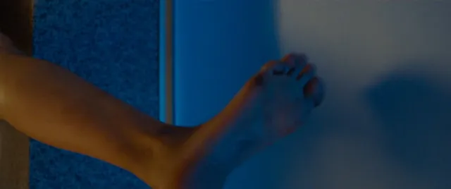 Maika Monroe showing a bare foot against a blue background in a scene.