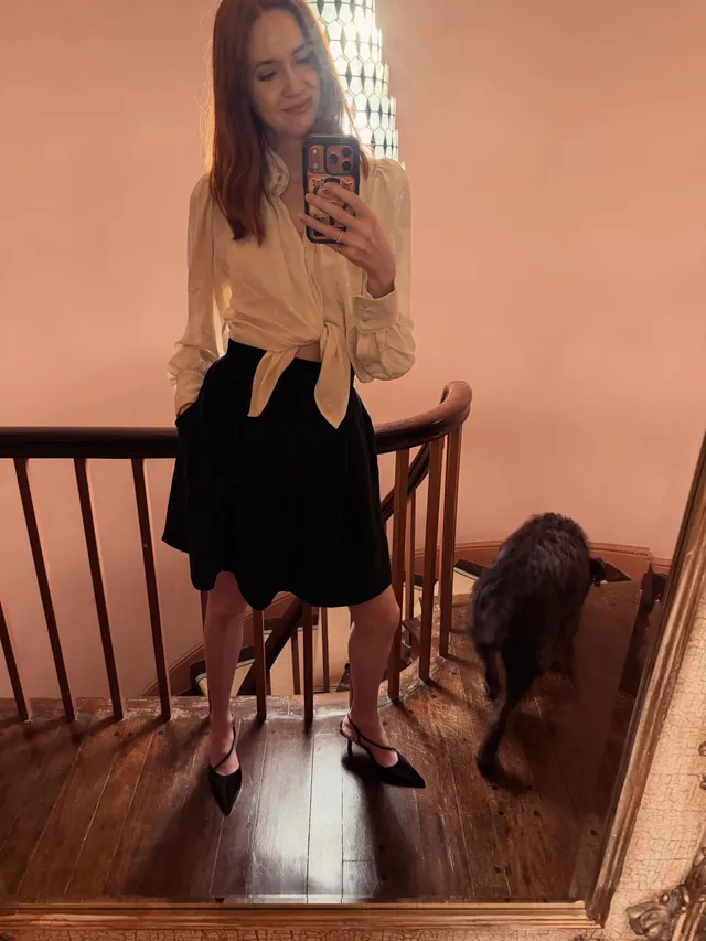 Karen Gillan posing beside a mirror wearing a black skirt and heels.