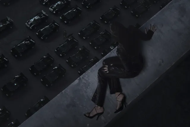 Lisa (Lalisa Manobal) sitting on a high ledge in heels above a city at night.