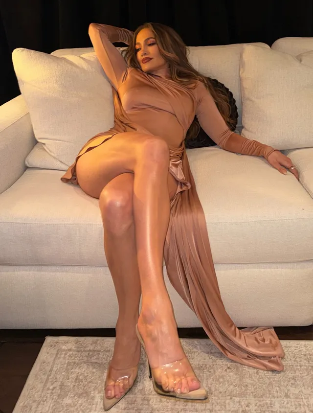 Jennifer Lopez a seated tan dress and transparent heels.