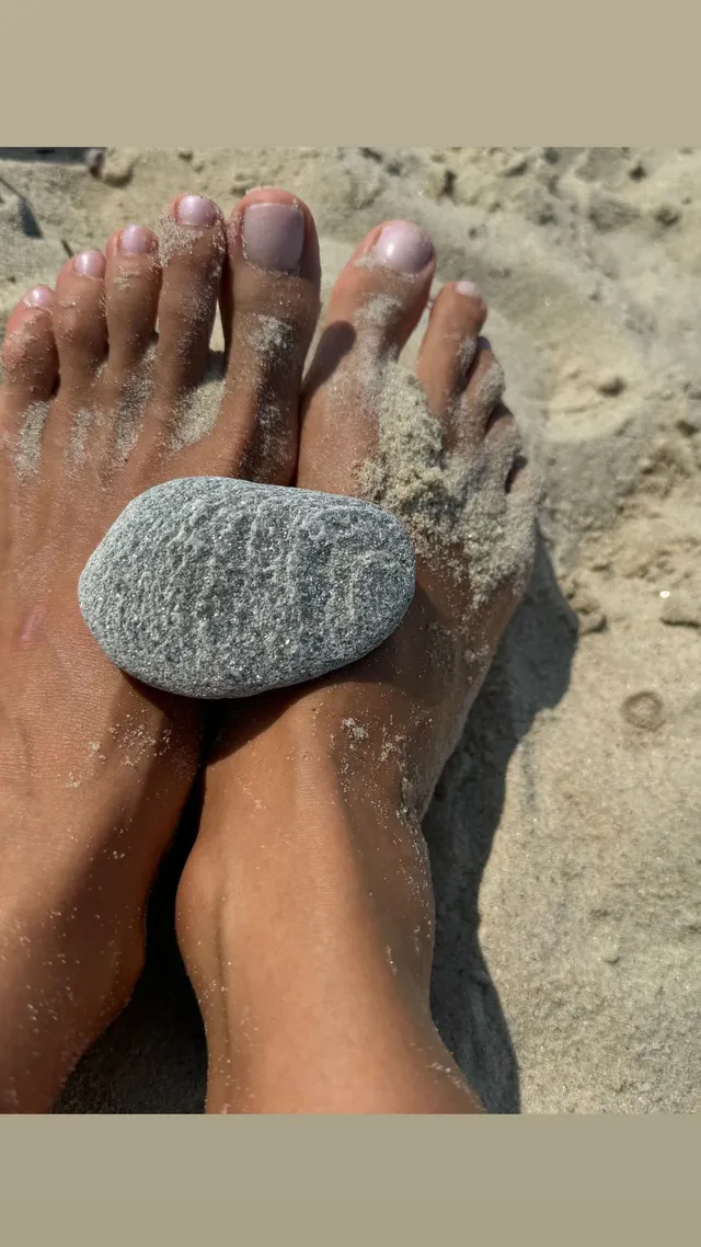 Irina Shayk bare feet with a smooth stone on a sandy beach.