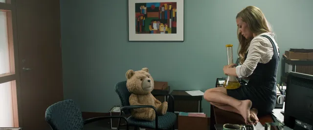 Amanda Seyfried sitting barefoot beside a teddy bear indoors.