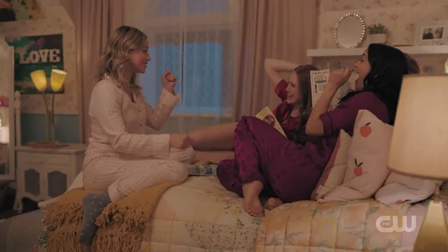 Camila Mendes sitting cross legged on a bed in a television scene.
