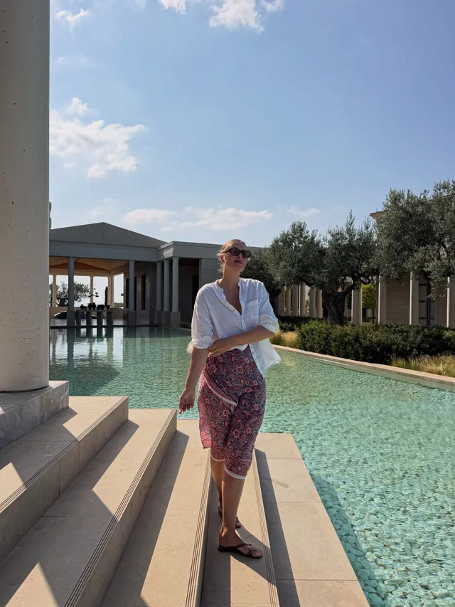 Maria Sharapova standing in flat sandals and a patterned skirt beside a swimming pool.