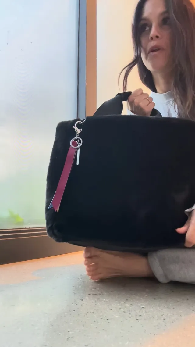 Rachel Bilson sitting cross-legged indoors holding a bag.