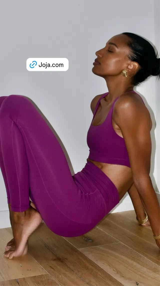 Jasmine Tookes stretching barefoot on a wooden floor in a purple exercise outfit.