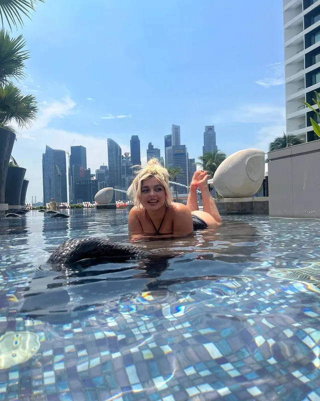 Bebe Rexha reclining in a pool with bare feet raised.