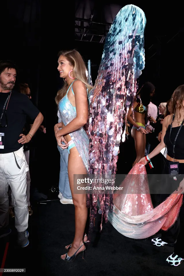Gigi Hadid walking backstage in pastel wings and heeled sandals.