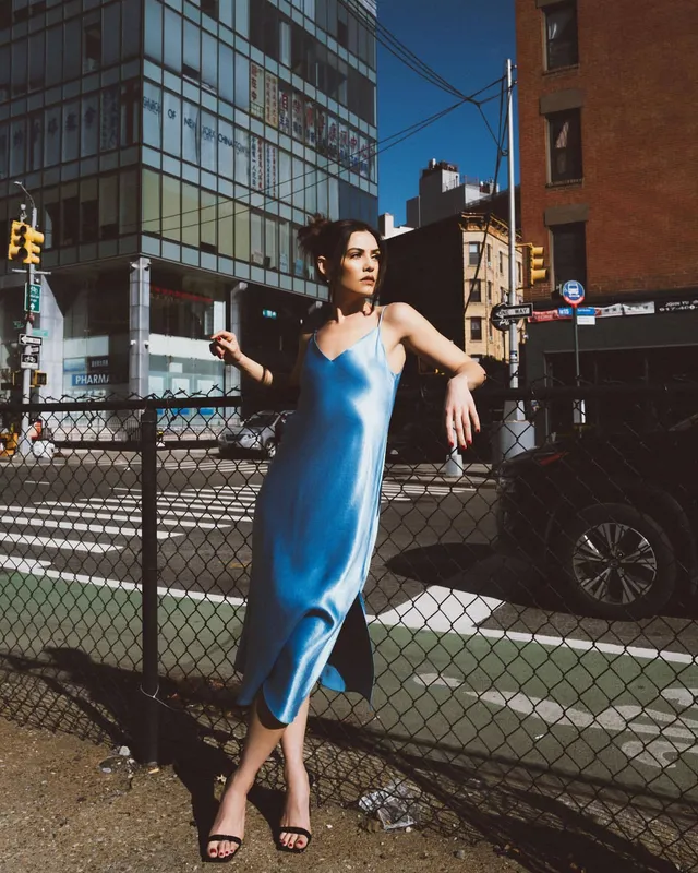 Danielle Campbell posing beside a fence in a blue satin dress.
