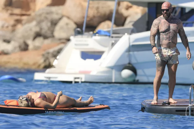 Bebe Rexha reclining barefoot on a paddleboard at sea.