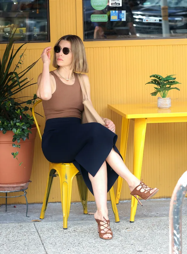 Jessica Biel sitting at a yellow table wearing brown heeled sandals.
