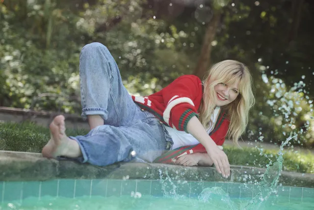 Kirsten Dunst resting barefoot beside a swimming pool in jeans.