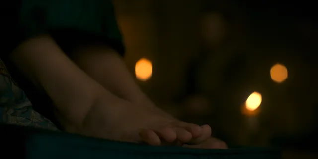 Olivia Cooke resting bare feet beside a candle in a screen scene.