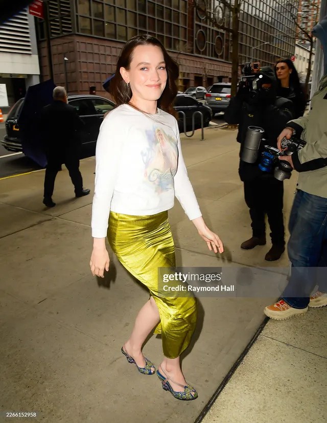 Victoria Pedretti walking on a city pavement in a green skirt.