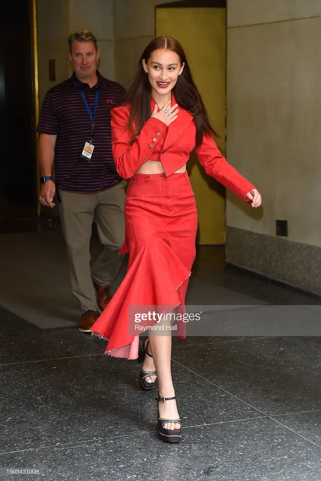 Lola Tung walking through a doorway in a red outfit and black heels.