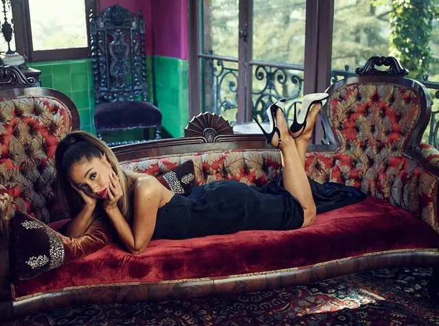 Ariana Grande lying on a red sofa with her shoes raised.