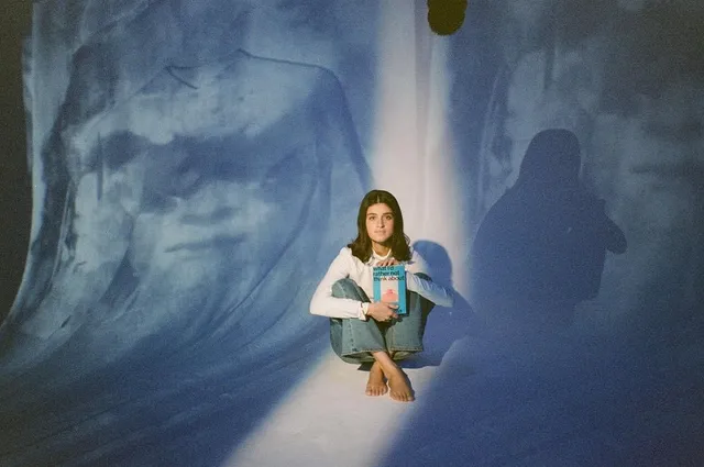 Anya Chalotra sitting barefoot against a blue studio backdrop.