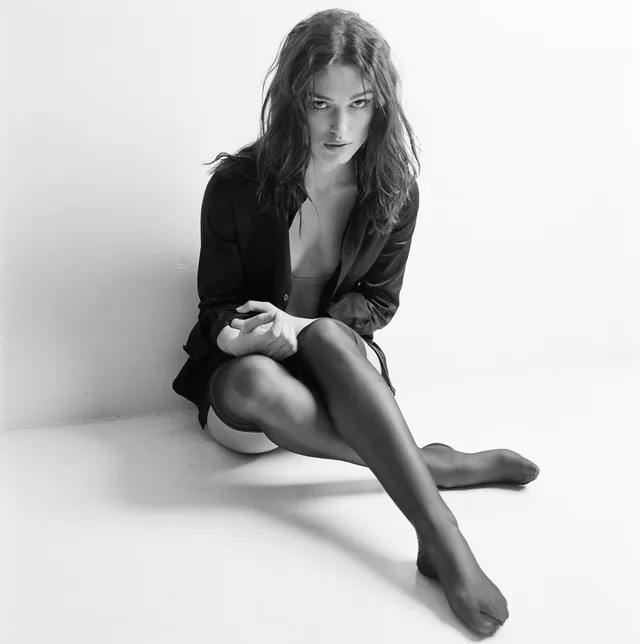 Keira Knightley a monochrome studio portrait in a dark outfit and sheer tights.