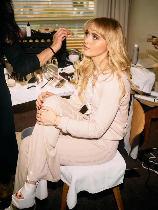 Kathryn Newton having makeup applied while wearing white platform heels.