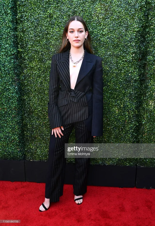 Victoria Pedretti posing on a red carpet in a dark tailored outfit.