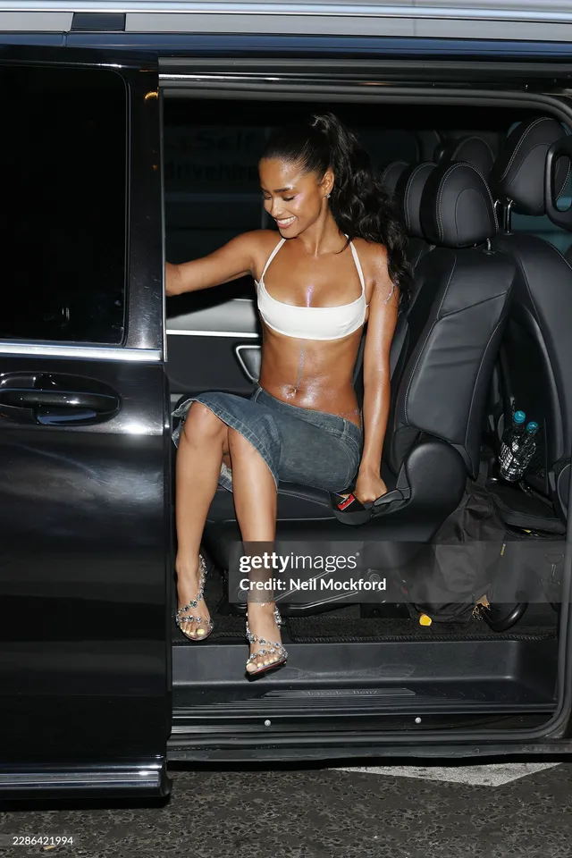 Tyla sitting in an open vehicle doorway in embellished heels and a denim skirt.