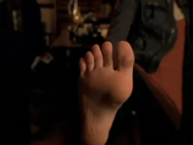 Kristen Bell with a bare sole visible beside a dark shoe in a screen image.