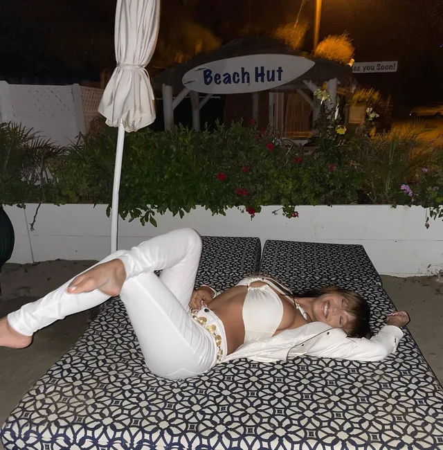Sierra Capri reclining barefoot on an outdoor lounger in a white outfit.