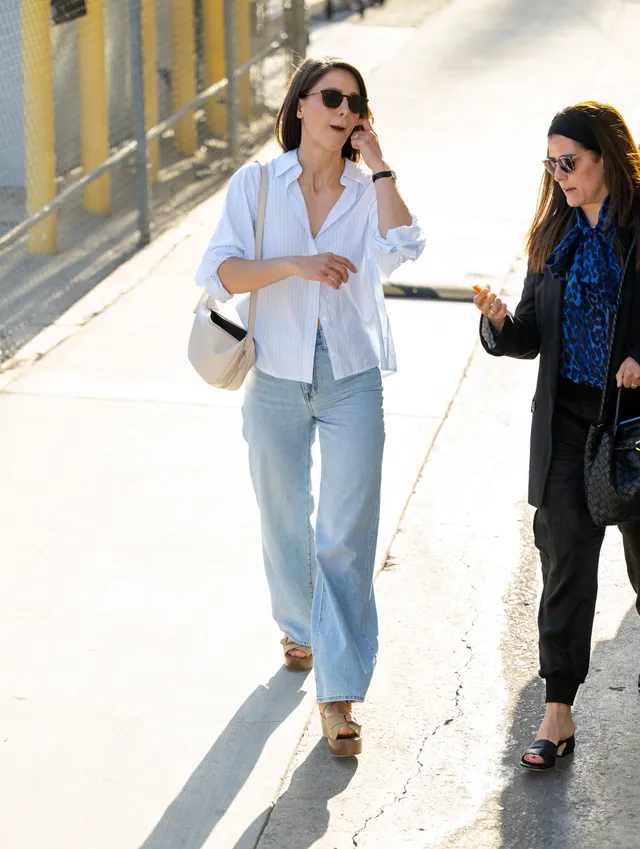 Melissa Benoist walking in a white blouse and jeans with tan wedge heels.