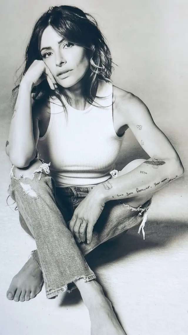 Sarah Shahi sitting for a black-and-white portrait in jeans and a white top.