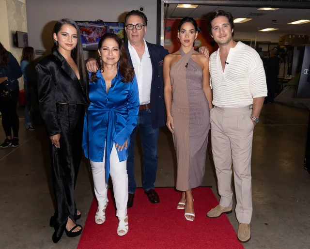 Adria Arjona posing with a group in a beige dress and pale heels.