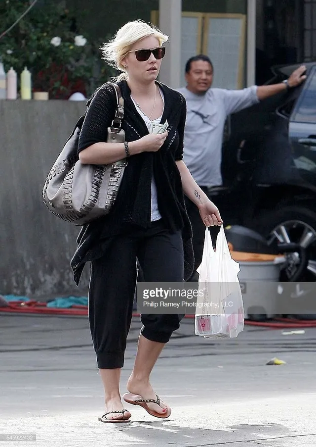 Elisha Cuthbert walking outdoors in cropped trousers and flip-flops.