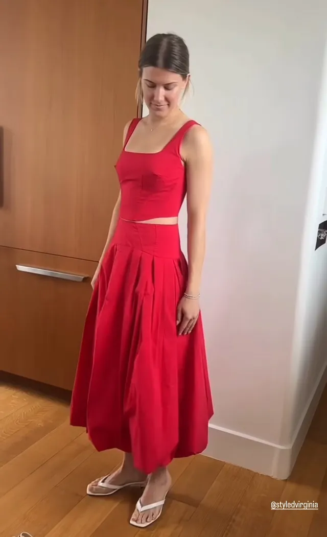 Eugenie Bouchard wearing white heeled sandals with a flowing red outfit indoors.