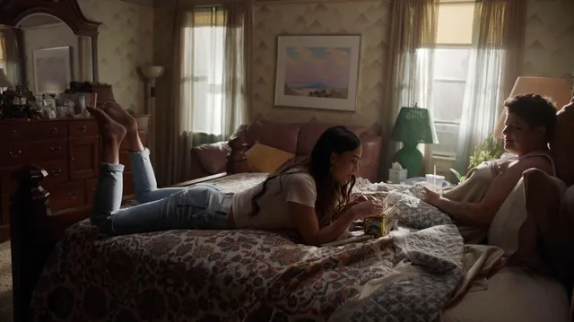 Melissa Barrera lying on a bed beside another person in a film scene.