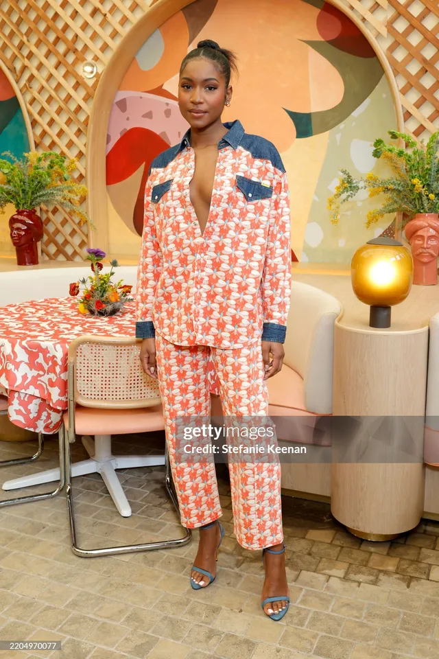 Carlacia Grant posing in a patterned trouser suit and blue heels indoors.
