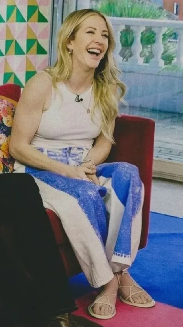 Ellie Goulding sitting in a colourful television studio in patterned trousers and flip-flops.