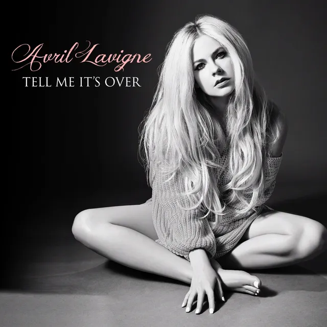 Avril Lavigne sitting cross-legged on a studio floor in a monochrome photograph.