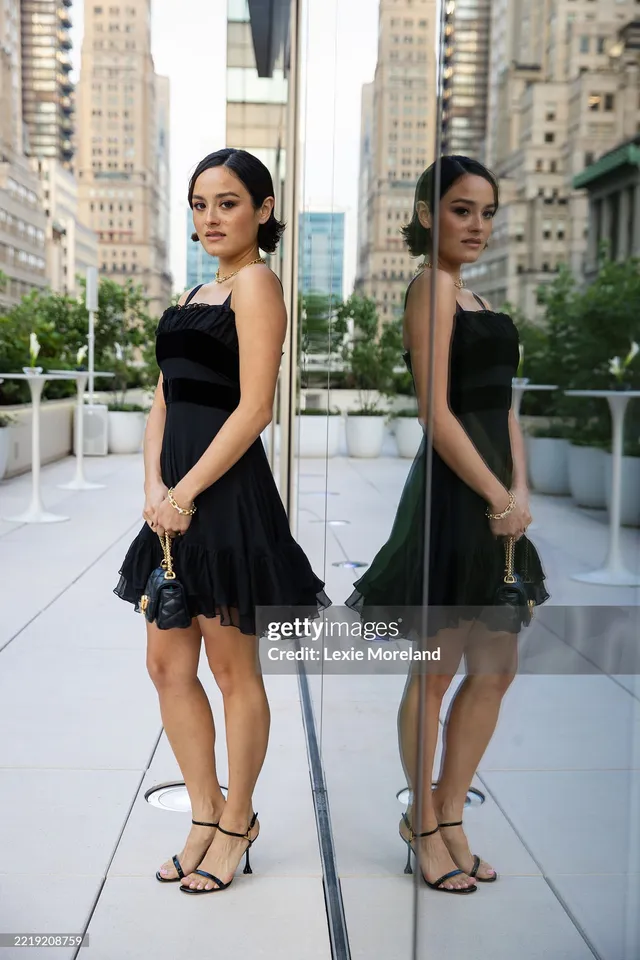 Chase Sui Wonders wearing a black dress and strappy heels beside a mirror.