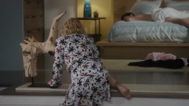 Kristen Bell sitting barefoot beside a bed in a screen image.