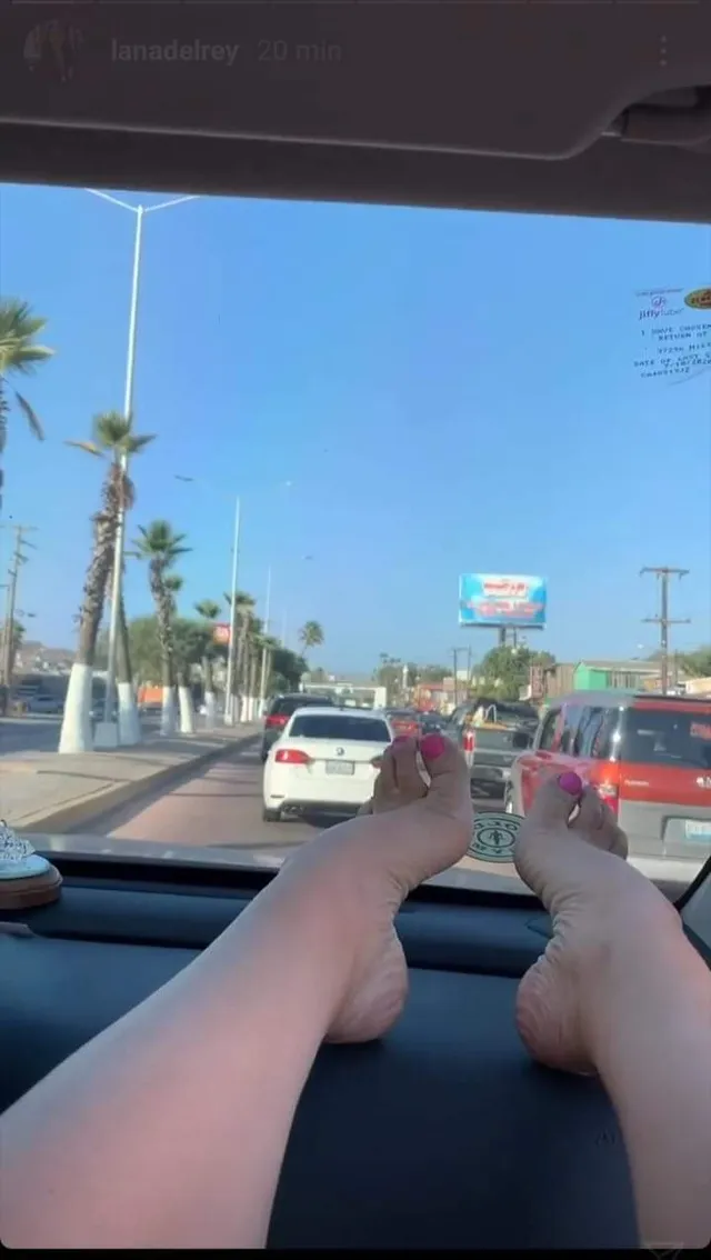 Lana Del Rey resting her bare feet on a car dashboard.