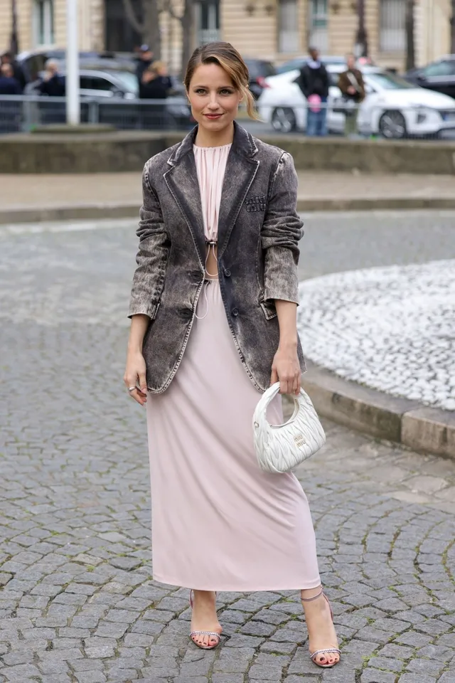 Dianna Agron posing outdoors in a jacket and pale skirt.