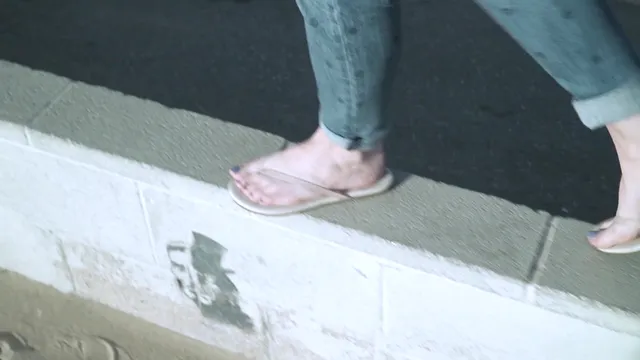 Elisha Cuthbert walking in pale flip-flops beside a pavement.