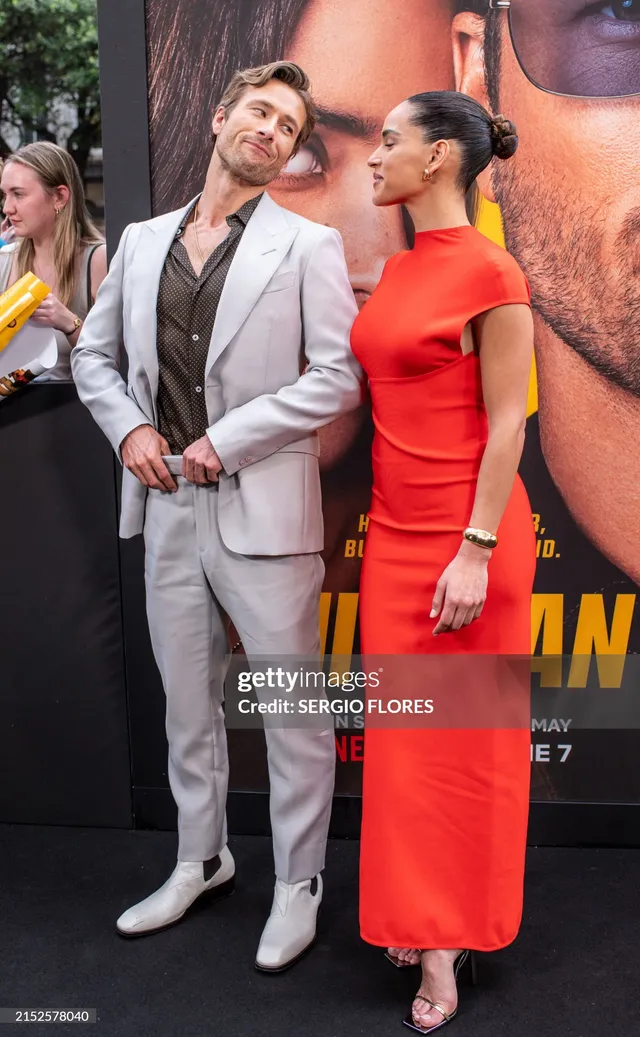 Adria Arjona posing beside a man in a red dress and pale heels.