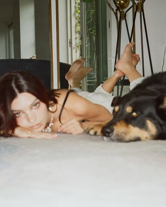 Emily Ratajkowski lying barefoot on a bed beside a dog.