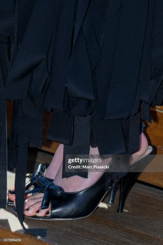 Jisoo showing black slingback heels beneath a dark skirt.