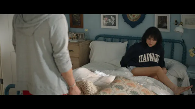Emily Alyn Lind sitting on a bed in a dark sweatshirt in a scene.