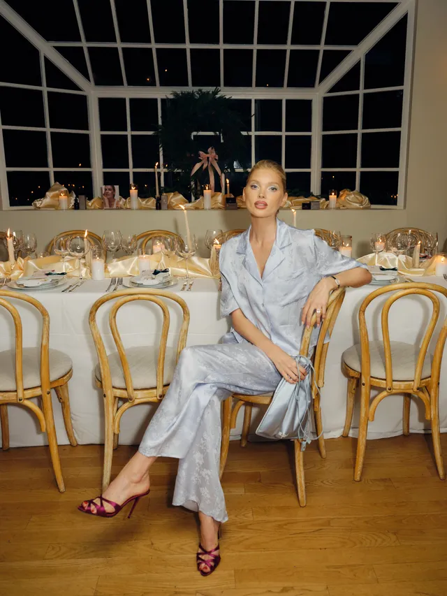 Elsa Hosk sitting at an event table in a pale blue outfit and burgundy heels.