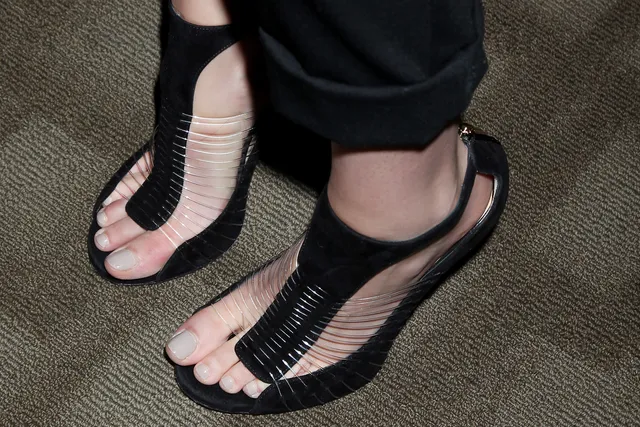 Kristen Stewart showing contrasting black and pale heeled sandals indoors.