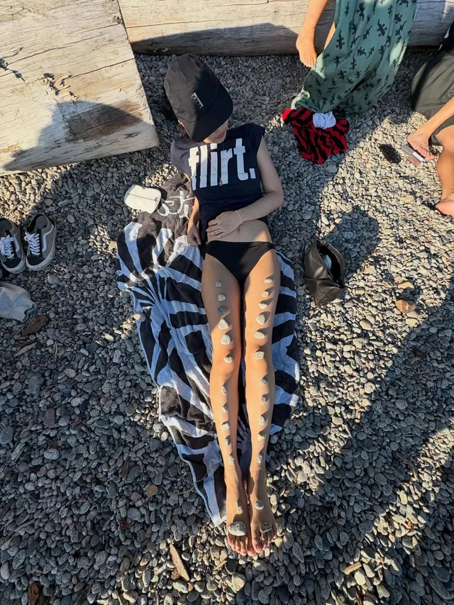 Jennie Kim reclining barefoot on a beach towel in a black T-shirt.