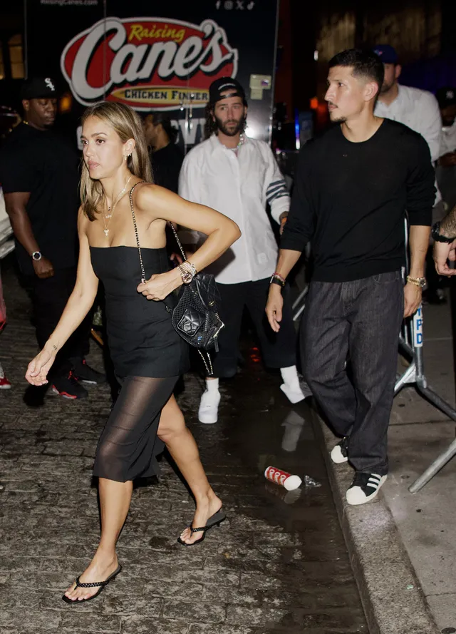 Jessica Alba walking with a group wearing a black dress and flip flops.