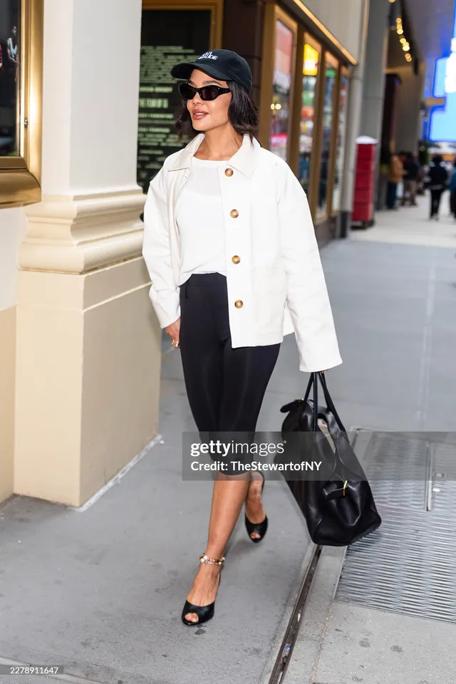 Tessa Thompson standing on a sidewalk in a white jacket.